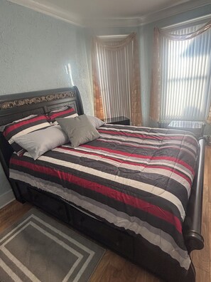 A bed with a striped bedspread, a headboard with a decorative pattern, and a bedside table with a lamp.
