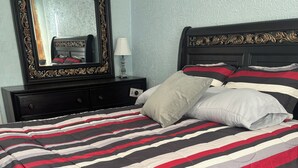 A bed with a striped bedspread, a nightstand with a lamp, and a mirror on the wall.