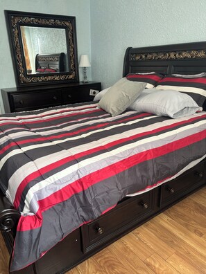 A bed with a striped bedspread, a nightstand with a lamp, and a mirror on the wall.