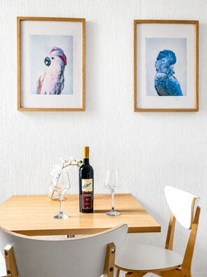 Un tavolo da pranzo con due quadri raffiguranti uccelli, una bottiglia di vino e due bicchieri.