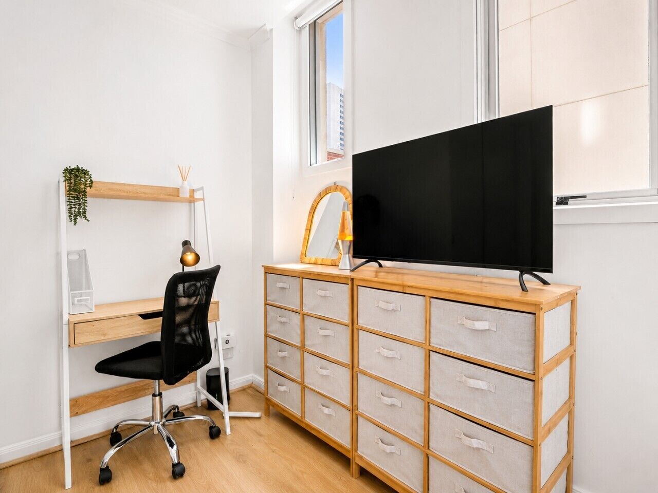 A room with a desk, chair, TV, and storage unit.