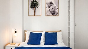 Um quarto com uma cama, duas almofadas, um abajur e duas fotos emolduradas na parede.