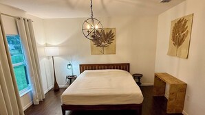 A bedroom with a large bed, a bedside table, a lamp, and artwork on the walls. - Peaceful 4-BR resting place (North Port)