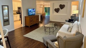 A living room with a TV, a glass coffee table, and a sofa. There is a kitchen visible in the background. - Peaceful 4-BR resting place (North Port)