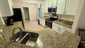 A kitchen with granite countertops, stainless steel appliances, white cabinets, and a double sink. - Peaceful 4-BR resting place (North Port)