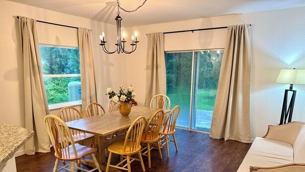 A dining area with a wooden table and chairs, a chandelier, and a view through large windows. - Peaceful 4-BR resting place (North Port)