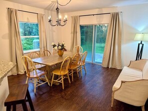 A dining area with a wooden table and chairs, a chandelier, and a view through large windows. - Peaceful 4-BR resting place (North Port)