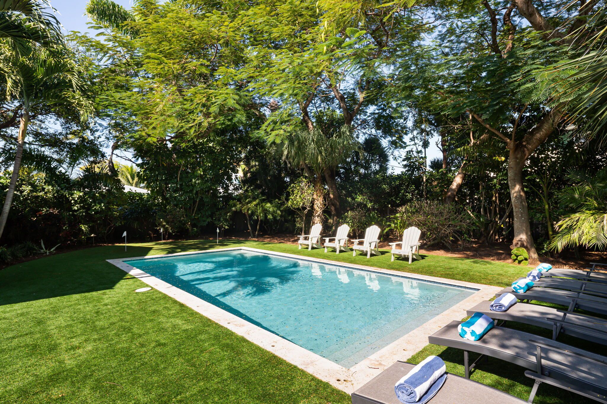 A rectangular swimming pool surrounded by a well-maintained lawn, with white lounge chairs and towels arranged for relaxation.