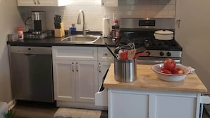 A modern kitchen with white cabinets, a stainless steel microwave, and a stove. There is a sink with a faucet, a coffee maker, and a bowl of apples on the counter. - Newly Remodeled 2BR 2BA Home  Close to Barrington (Barrington)