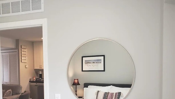 A bedroom with a round mirror, a bed with a patterned pillow, and a framed picture on the wall. - Newly Remodeled 2BR 2BA Home  Close to Barrington (Barrington)
