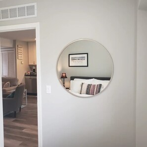 Une chambre avec un miroir rond, un lit avec un coussin à motifs et un tableau encadré au mur.