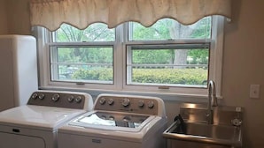 A laundry room with two washers and a dryer, a sink, and a window with a view of greenery. - Newly Remodeled 2BR 2BA Home  Close to Barrington (Barrington)
