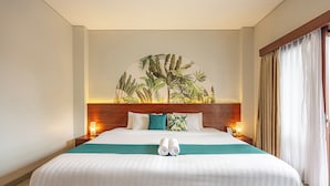 A hotel room with a large bed, a headboard with a tropical mural, two bedside lamps, and a view of the beach through the window.