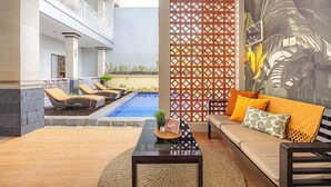 A modern lounge area with a pool, a sofa with cushions, a coffee table, and a decorative wall with a tropical mural.