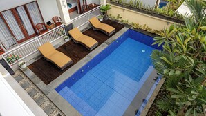 A swimming pool with lounge chairs, a wooden deck, and potted plants.