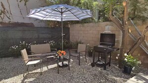 An outdoor patio with a striped umbrella, a table with chairs, a small table with a TV, and potted plants. - Charming & Cozy Home Near Caltech PCC & Pasadena Convention Center King-size bed (Pasadena)