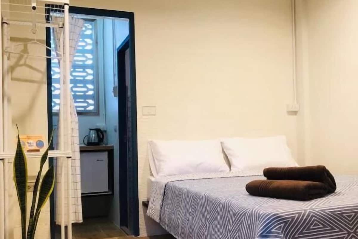 Ein Schlafzimmer mit Bett, Nachttisch, Topfpflanze und einem durchgegangenen Tür sichtbaren Badezimmer.