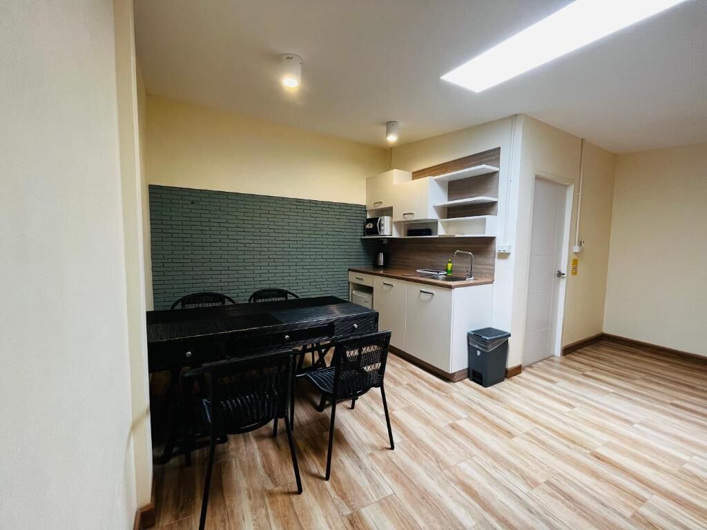 Cocina compacta con comedor, que incluye una mesa y sillas negras, un microondas y un cesto de basura pequeño.