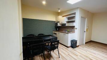 Cocina compacta con comedor, que incluye una mesa y sillas negras, un microondas y un cesto de basura pequeño.