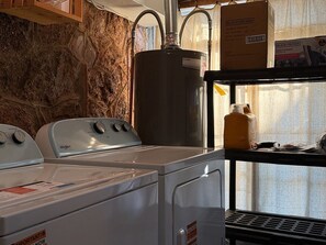 Een wasruimte met een wasmachine en droger, een grote boiler en een plank met schoonmaakmiddelen.