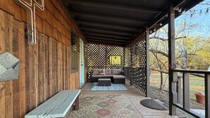 En overdækket veranda med en bænk, siddepladser med hynder og et espalier.