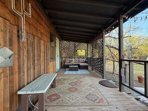 Een overdekte veranda met een bank, een zithoek met kussens en een lattenhek.