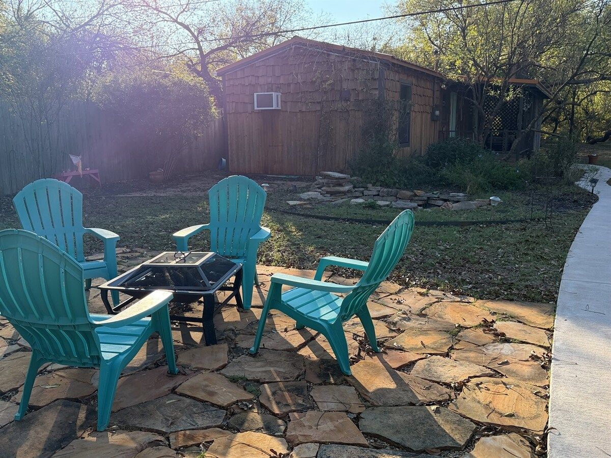 Un patio con cuatro sillas y una mesa, un cobertizo de madera y un sendero de piedra.