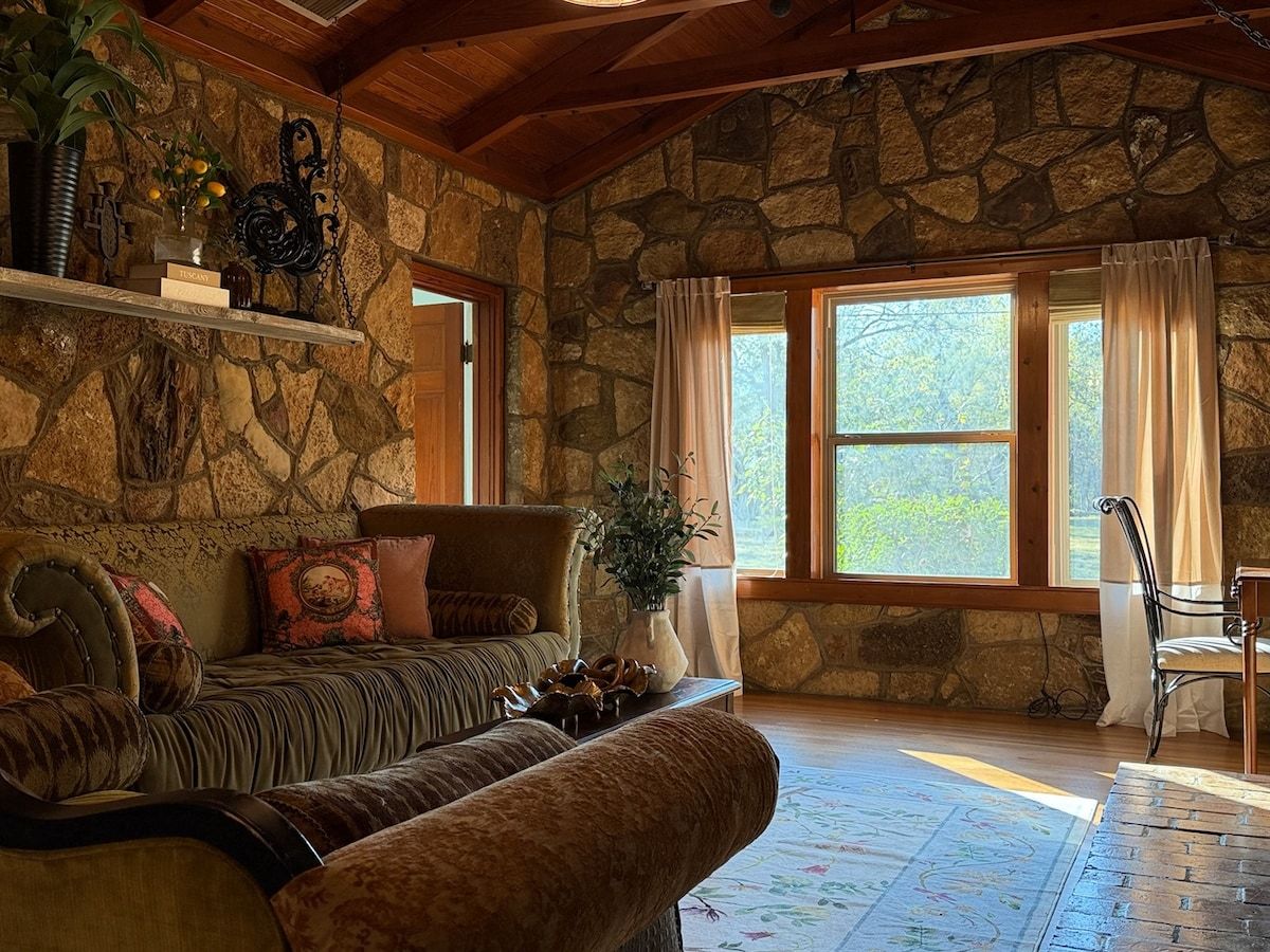 A cozy room with a stone wall, a sofa, a chair, and a large window with curtains.