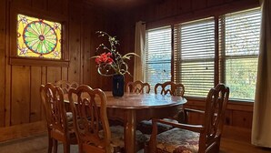 Et spisekammer i træ med et rundt bord og stole, et farvet glasvindue og en vase med blomster.