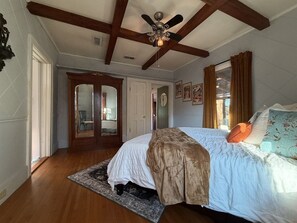 A bedroom with a large bed, wooden flooring, a ceiling fan, and a view of a hallway. - La Dolce Vita - Rustic Italian-Inspired Retreat (Abilene)