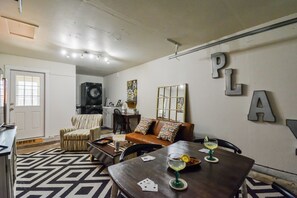 Sala de estar con sofá, mesa de centro y mesa de comedor con cartas y bebidas. Se ve una lavadora al fondo.