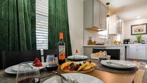 Mesa de jantar posta com pratos, talheres e uma garrafa de vinho, com cozinha ao fundo.