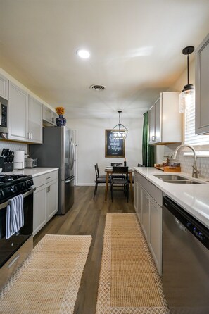 A modern kitchen with stainless steel appliances, a dining area with a table and chairs, and a hanging light fixture. - Red Bud Run - Stylish Abilene Retreat (Abilene)