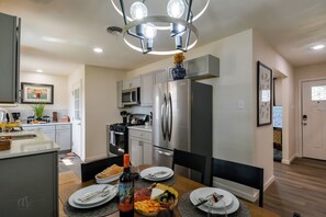 A modern kitchen with stainless steel appliances, a dining table set with plates and a bottle of wine, and a decorative ceiling light.