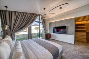 A modern hotel room with a large bed, a TV mounted on the wall, and a desk with a chair. - XO Canggu - Adults Only (Canggu)