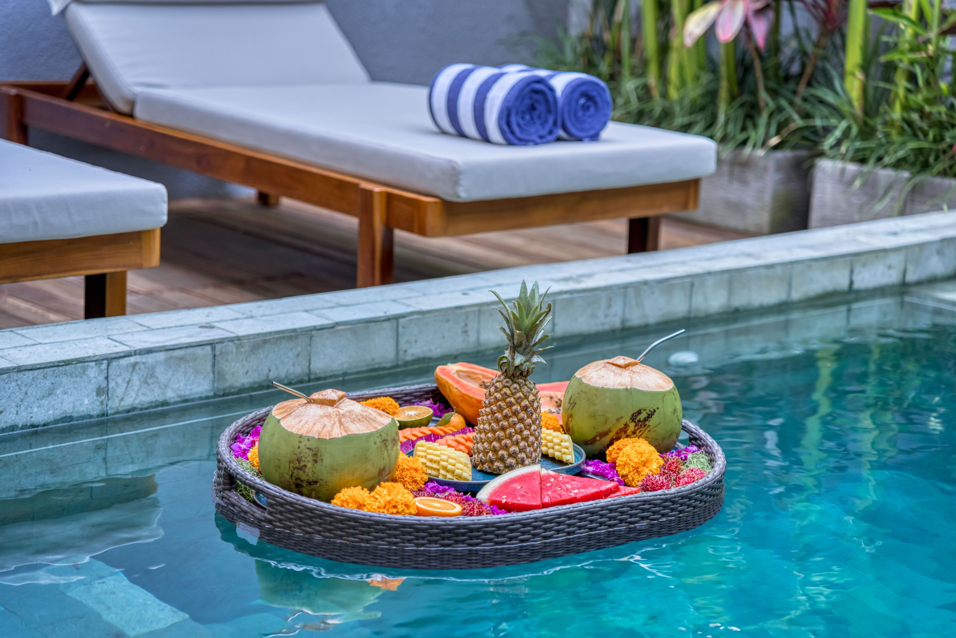Ein Poolbereich mit Liegestühlen, einer schwimmenden Frucht- und Blumenkomposition und einem Holzdeck.