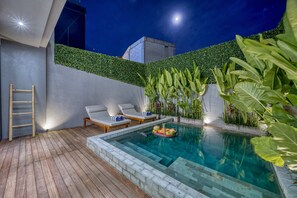 A pool area with a wooden deck, lounge chairs, and a small pool with floating plants. - XO Canggu - Adults Only (Canggu)