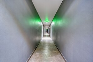 Un long couloir étroit, avec une signalétique de sortie verte à l’extrémité, bordé de murs sobres et doté d’un sol carrelé.