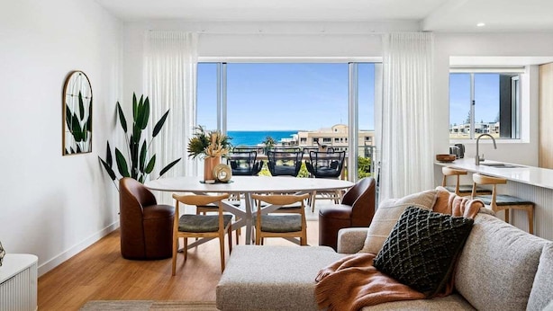 A modern living room with a dining area, large windows with a view of the sea, and a kitchen area. - Ocean Views Kings Beach (Kings Beach)