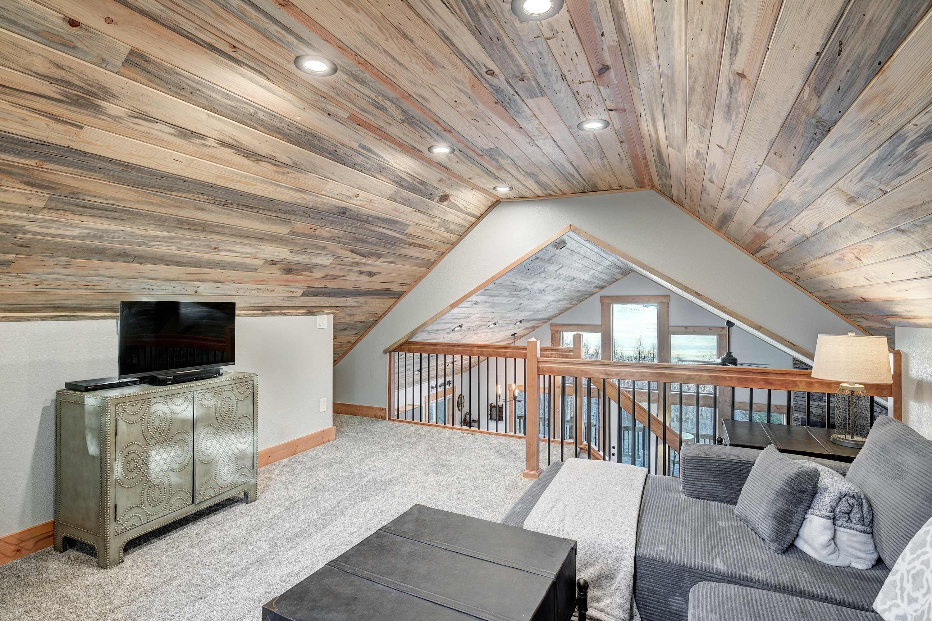 A loft-style room with a sloped ceiling, a television on a cabinet, a sofa, and a staircase leading to an upper level.