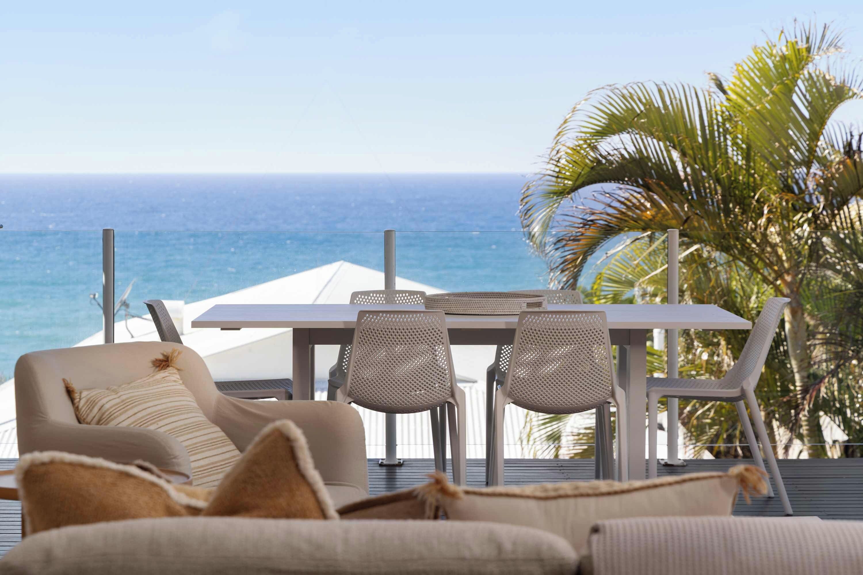A balcony with a table and chairs, overlooking the ocean.