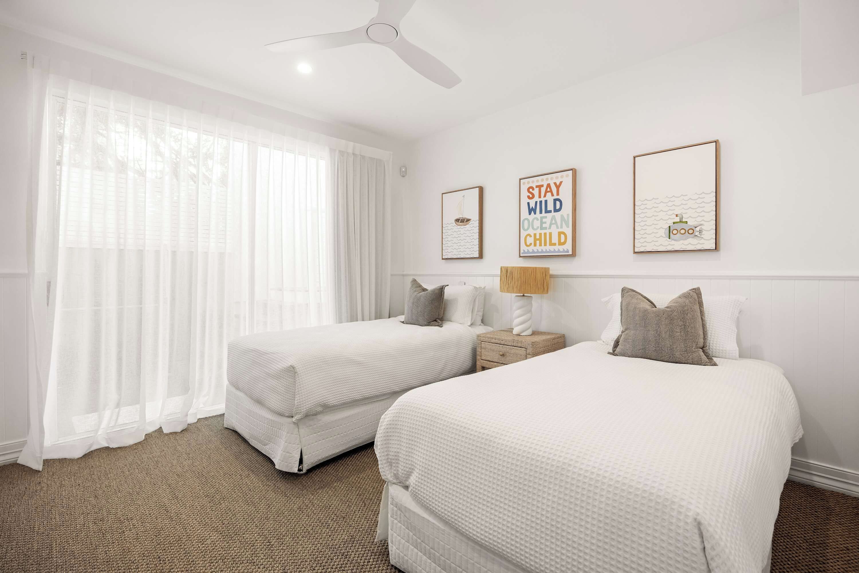 A hotel room with two beds, a ceiling fan, and artwork on the wall.