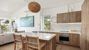 A modern kitchen with a large island, wooden cabinets, and a hanging light fixture. - Thalasa Two at Sunshine Beach (Sunshine Beach)