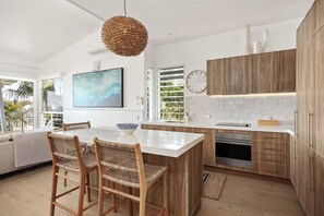 A modern kitchen with a large island, wooden cabinets, and a hanging light fixture. - Thalasa Two at Sunshine Beach (Sunshine Beach)