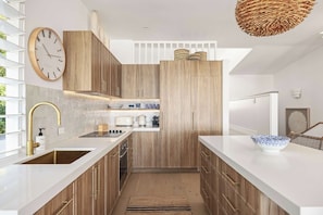 A modern kitchen with wooden cabinets, a white countertop, and a large clock. - Thalasa Two at Sunshine Beach (Sunshine Beach)