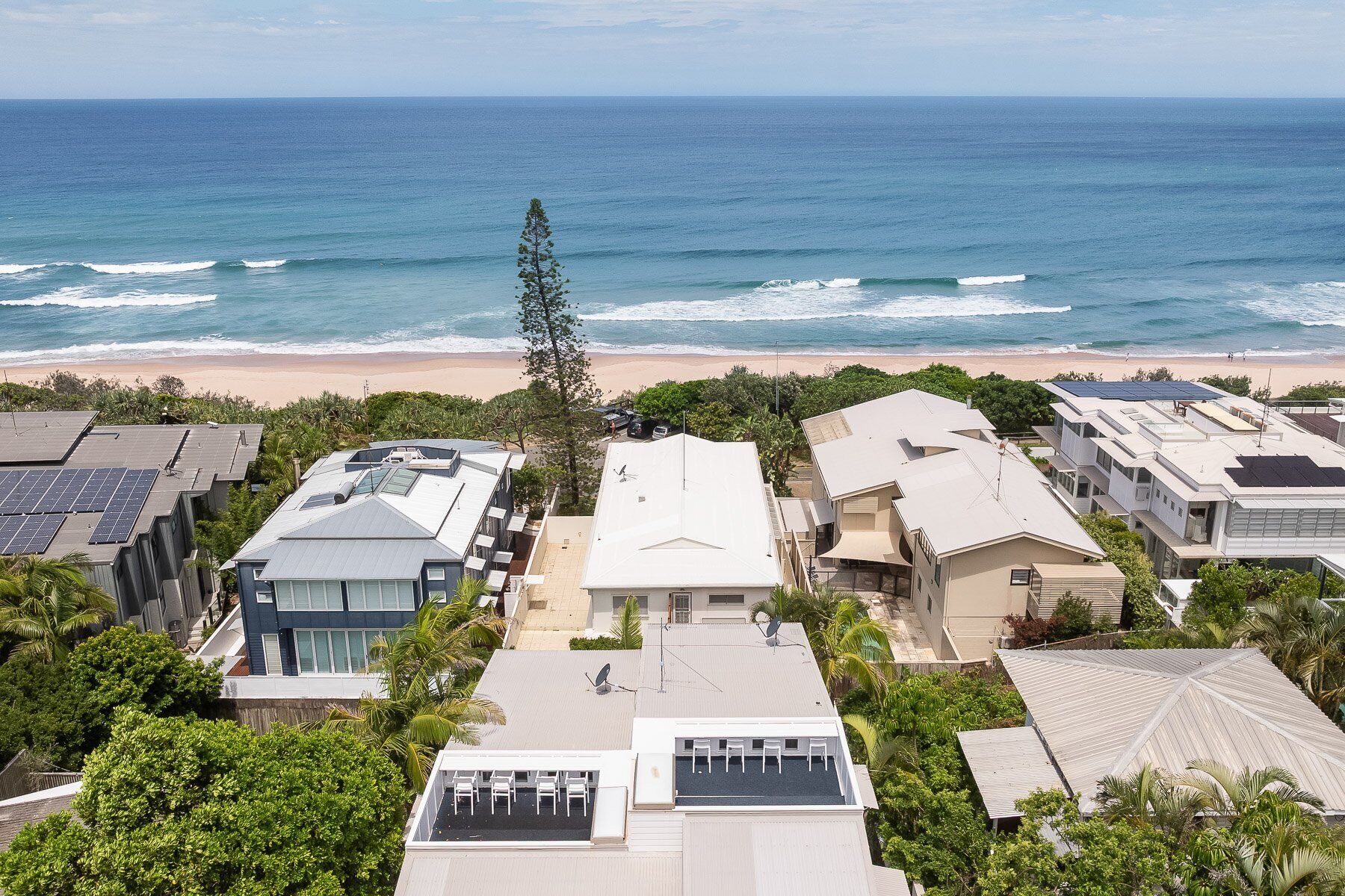 Un barrio residencial con casas, algunas con paneles solares, con vistas a una playa y al océano.