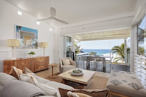 A modern living room with a view of the ocean, a ceiling fan, and a dining area with outdoor seating. - Thalasa Two at Sunshine Beach (Sunshine Beach)