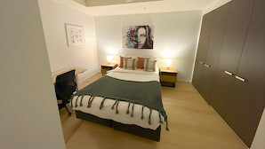 A bedroom with a bed, bedside tables, a desk, a wardrobe, and a painting on the wall. - Mega Style Apartments Tribeca (East Melbourne)