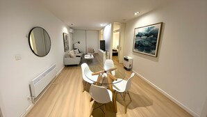 A modern living room with a dining area, a sofa, a TV, and a large abstract painting. - Mega Style Apartments Tribeca (East Melbourne)