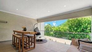 Un balcón moderno con una mesa y sillas de madera, una silla colgante y vistas a abundante vegetación.